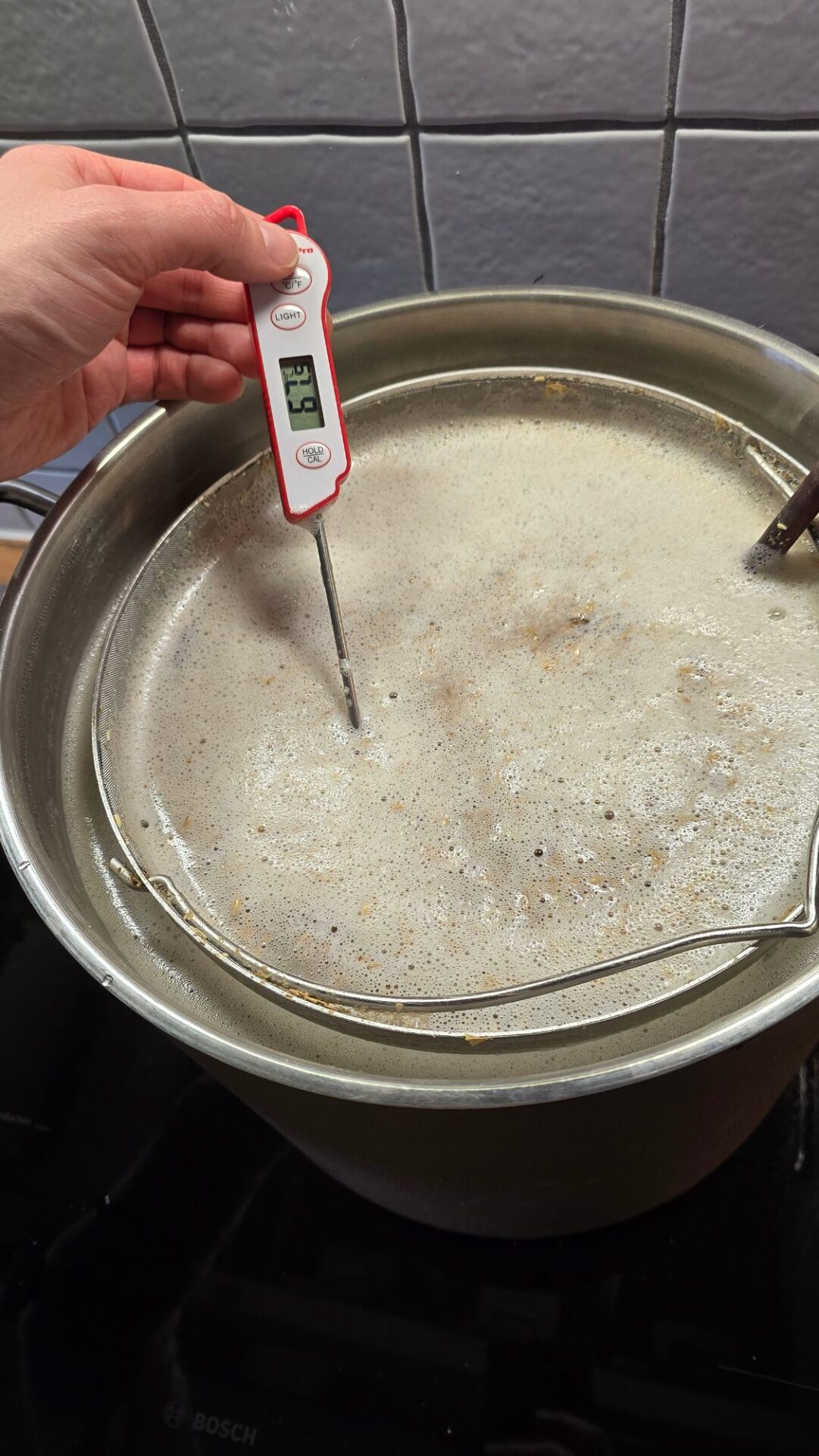 Digitalthermometer misst die Temperatur der schäumenden Maische im Topf mit eingehängtem Sieb auf dem Herd