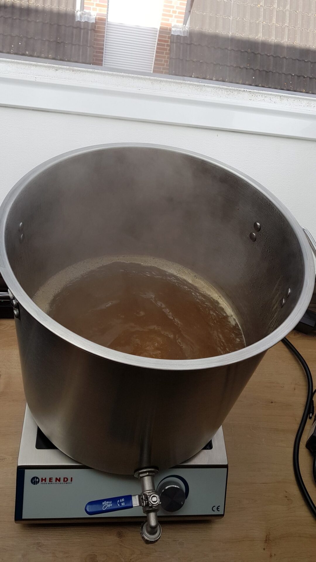 Kochende Würze dampft beim Bierbrauen in einem Edelstahltopf mit Auslaufhahn auf einem Hendi Induktionskocher