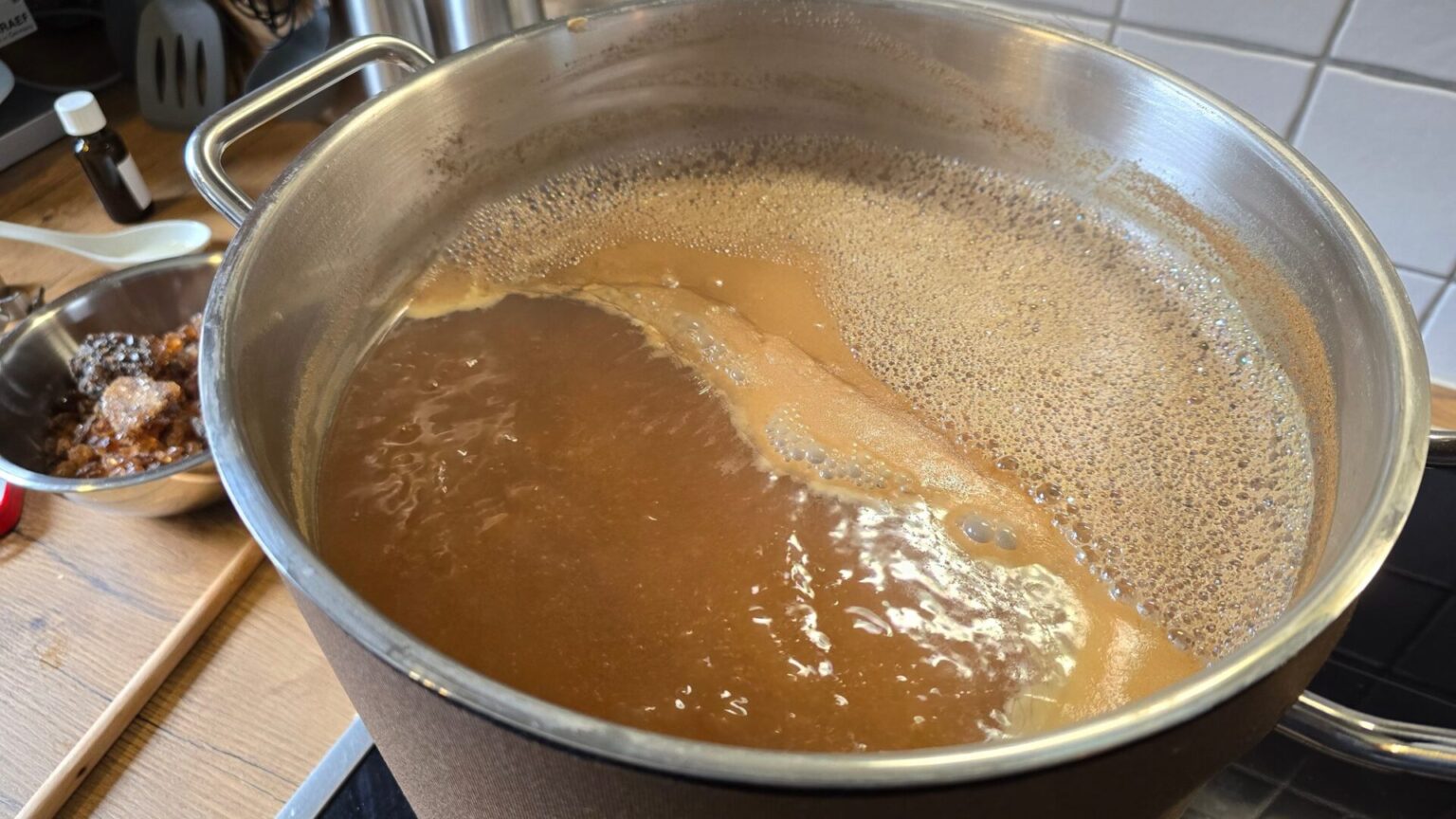 Kochende Würze mit Schaum im Edelstahltopf, daneben eine Schale mit braunem Kandiszucker für ein Quadrupel