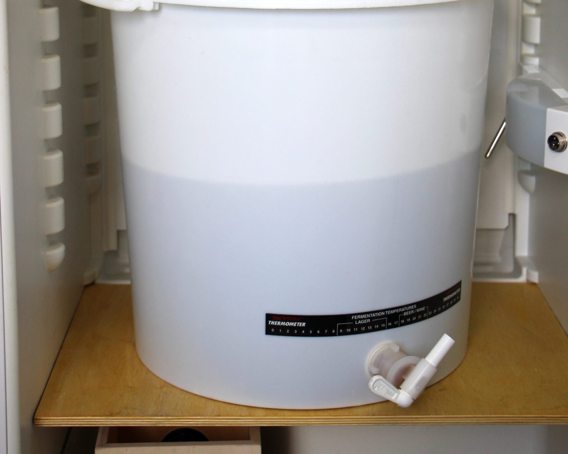 Weißer Gäreimer mit Hahn im Gärschrank, am Eimer ein Thermometerstreifen mit Gärtemperaturen für obergäriges und untergäriges Bier